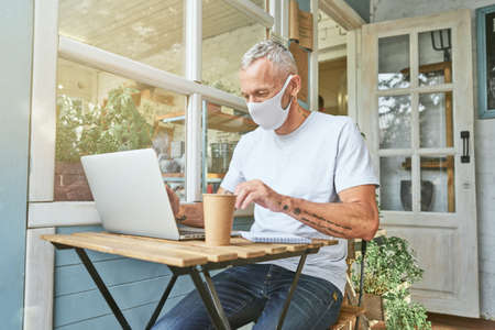 Caucasian businessman in protective mask working on laptopの写真素材