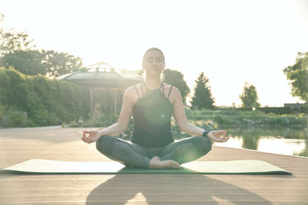 Quiet mind. Relaxed middle aged woman meditating, sitting in Lotus pose while doing yoga on a mat in a green parkの写真素材