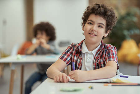 Diligent little school boy listening to his teacher while sitting at the desk in classroomの写真素材