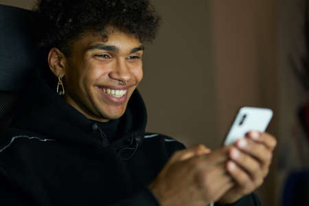 Close up portrait of smiling young handsome guy texting, chatting with friends, using smartphone late at night at homeの写真素材