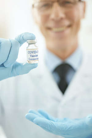 Doctor hand in sterile glove holding bottle of covid-19 vaccineの写真素材