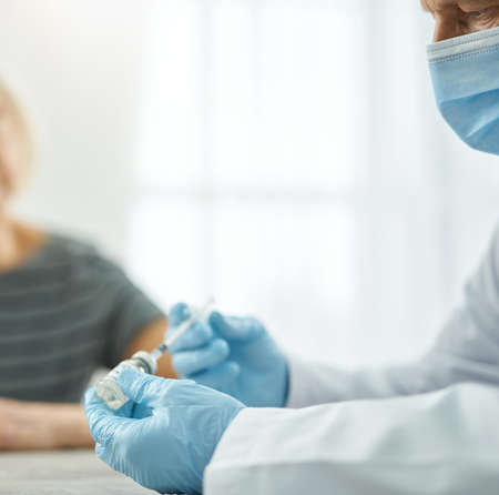 Male doctor in sterile gloves filling syringe with vaccineの写真素材