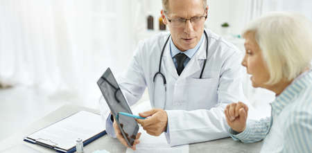 Male doctor using tablet computer and talking with patient in clinicの写真素材