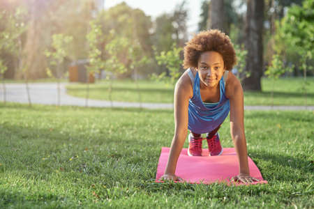 Joyful little girl doing plank on yoga mat in parkの写真素材