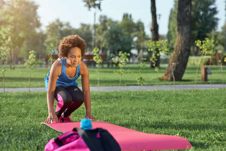 Adorable Afro American girl rolling out yoga mat on grassの写真素材