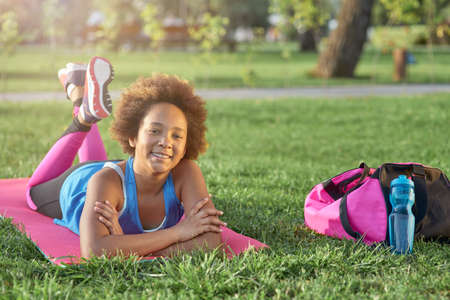 Cheerful little girl lying on yoga mat outdoorsの写真素材