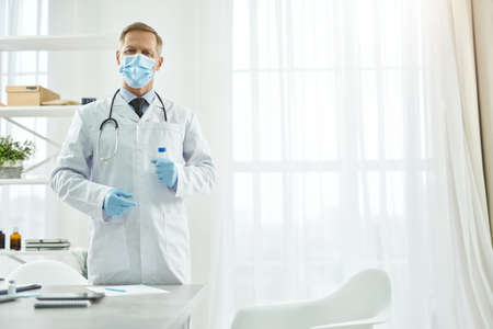 Male doctor in medical mask holding test tubeの写真素材