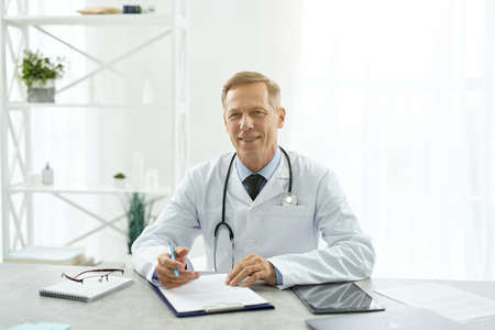 Cheerful male doctor sitting at the table in clinicの写真素材