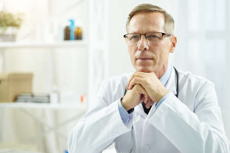 Handsome doctor in glasses resting his chin on handsの写真素材