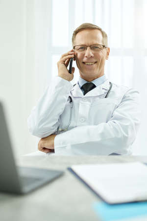 Cheerful male doctor talking on mobile phone at workの写真素材