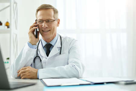 Cheerful male doctor having phone conversation in clinicの写真素材