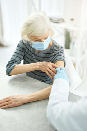 Old woman receiving injection of coronavirus vaccine in clinicの写真素材