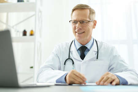 Cheerful male doctor using modern laptop at workの写真素材