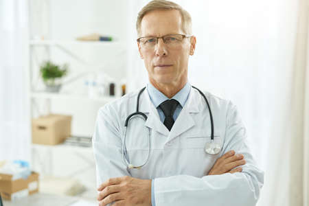 Handsome male doctor in lab coat standing in clinicの写真素材