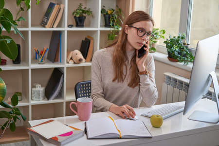 Busy lady sitting at the table while talking on phoneの写真素材