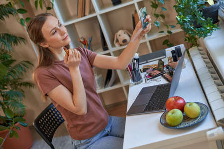 Beautiful lady applying lipstick during online makeup tutorialsの写真素材
