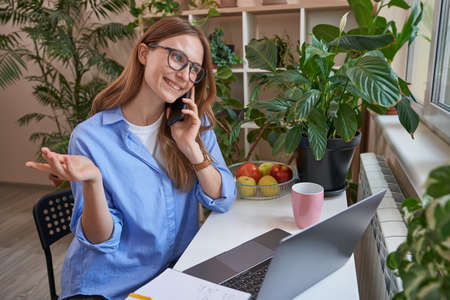Happy young woman using mobile phone at homeの写真素材