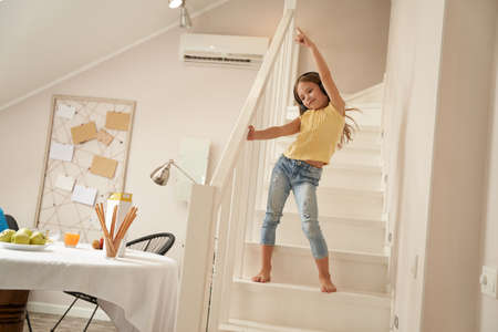 Cute little caucasian girl wearing headphones listening music and dancing on stairs at home, relax and leisure concept, happy childhoodの写真素材