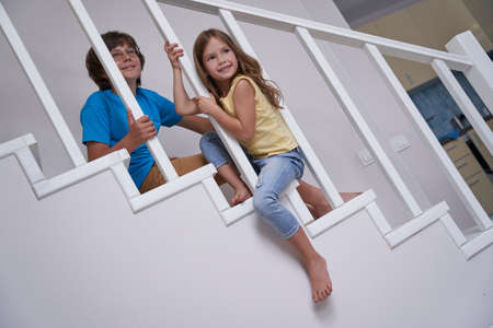 Little boy and girl, brother and sister sitting on the stairs at home and smiling, they are playing and having fun togetherの写真素材