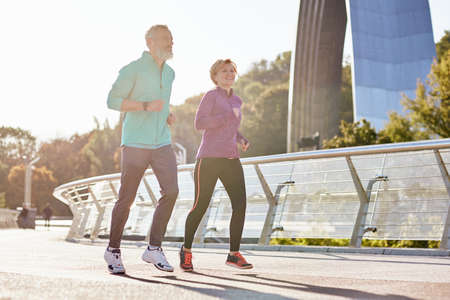 Healthy mind and body. Cheerful active mature couple in sportswear smiling while running on a sunny day. Joyful senior couple doing sport together outdoorsの写真素材