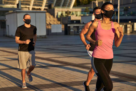 Three athletes in protective masks on their faces while joggingの写真素材