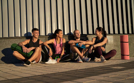 Happy four friends chatting after training outdoorsの写真素材