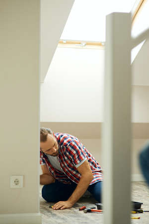 Handyman sitting on the floor while fixing smething in a room. Home repair hand tools on laminate flooringの写真素材