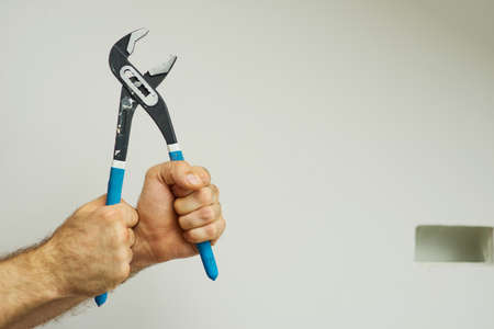 Hands of repairman holding a pipe wrench with blue handle over white backgroundの写真素材