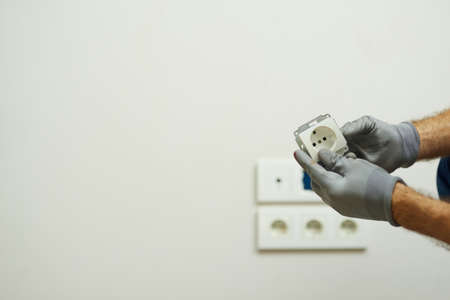 Close up shot of hands of electrician wearing protective gloves while installing wall plug socket in a new houseの写真素材