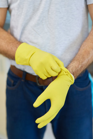 Get started. Close up shot of hands of man, professional male cleaner wearing gloves while getting ready for doing houseworkの写真素材