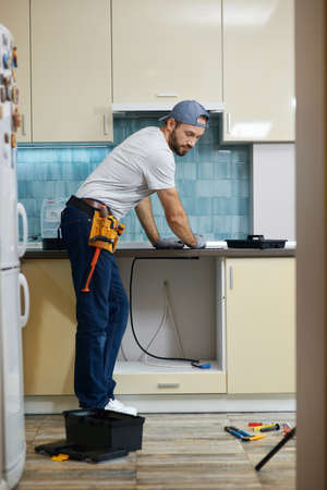 Full length shot of young repairman, professional plumber choosing the best tool for working. Tools and equipment on the floor in the kitchenの写真素材