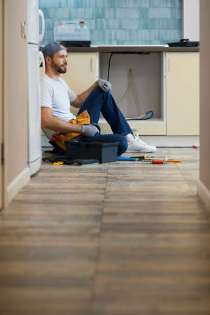 Full length shot of professional repairman with toolbox taking a break, sitting on the floor indoorsの写真素材