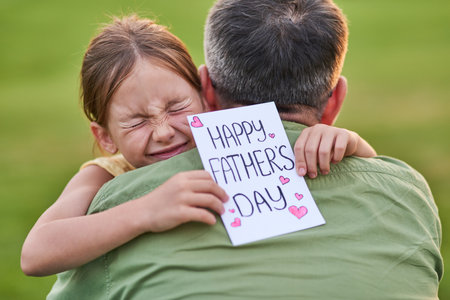 Love you daddy! Cute little girl looking emotional while greeting her dad and giving him handmade postcard, spending time together in the beautiful green parkの写真素材