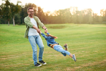 Young father playing and having fun with his little daughter in the beautiful green park on a summer dayの写真素材