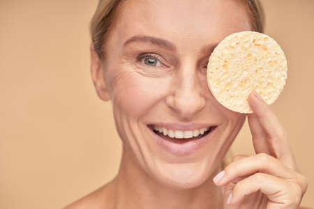 Happy mature lady holding sponge near her faceの写真素材