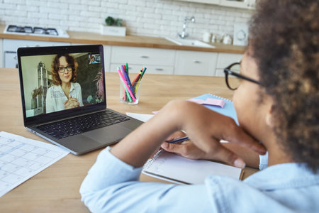 Young female teacher communicating with teen schoolgirl via video chat app while having online lesson during lockdownの写真素材