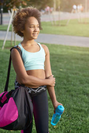 Cheerful little girl with bottle of water standing on the streetの写真素材