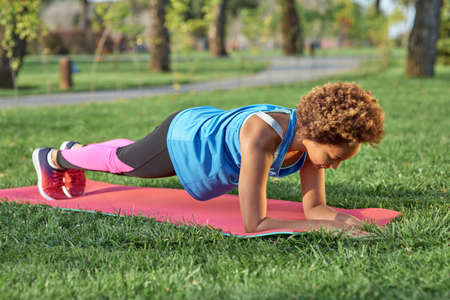Sporty Afro American girl doing plank on yoga mat in park