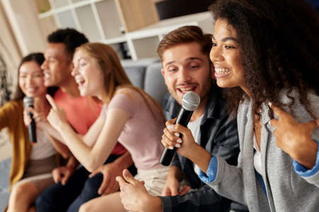 Friends and music. Joyful friends looking excited while playing karaoke at home, singing with...