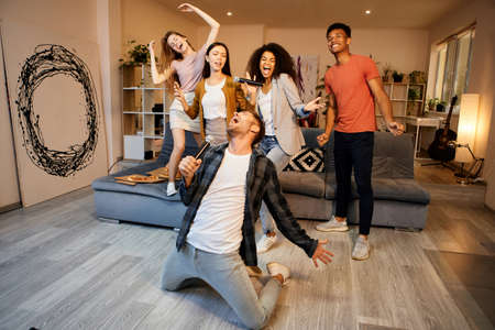 Vibrations for good fun. Full length shot of handsome young guy looking enthusiastic while singing with microphone, playing karaoke with friends in the modern apartmentの写真素材