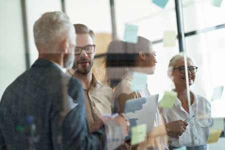 Group of multiracial coworkers standing in the modern office and putting colorful sticky notes on a...