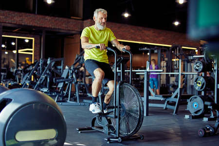 Cardio workout. Full length of a mature athletic man in sportswear doing cycling on exercise bikes at gymの写真素材