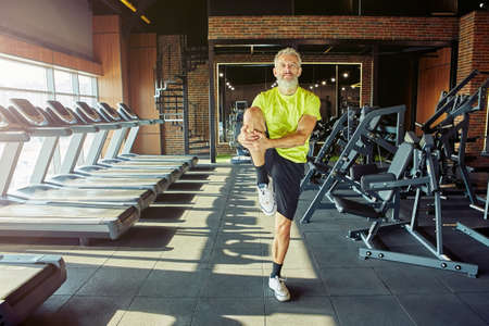 Stretching body. Portrait of athletic middle aged man in sportswear warming up before training in a gym or sport clubの写真素材