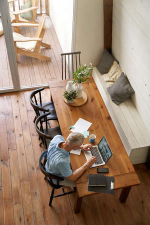 Top view of a mature caucasian businessman working at his modern apartment, using laptop while sitting at tableの写真素材