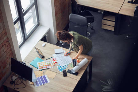 High angle view of interior designer or architect in casual wear with messy hairdo working with color samples and blueprint for new project, standing in her officeの写真素材