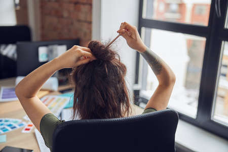 Back view of busy woman at work making a hair bun using wooden stick. Female hands and messy brown hairの写真素材