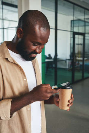 Handsome young man checking his smartphone during coffee breakの写真素材