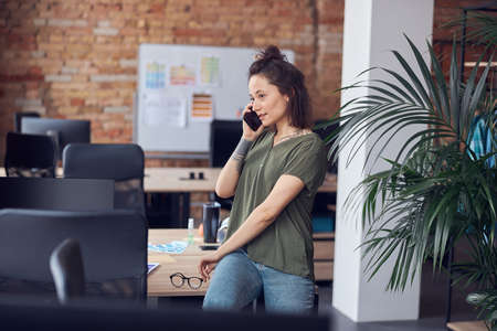 Young woman, architect or interior designer looking away while talking on the phone, standing in modern green office and discussing new projectの写真素材