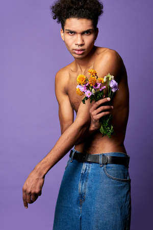 Portrait of sexy latino male posing with flowers in hand on purple background. Transgender nude torsoの写真素材