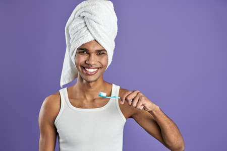 Young transgender man brushing teeth isolated on purple background portraitの写真素材